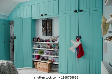 Wide angle view of a bedroom interior with a wardrobe and door partially open. There is also storage space and shelves in the middle between the two built in wardrobes.