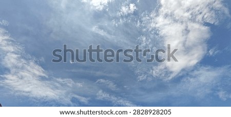 Wide angle view of bright blue sky with soft white clouds, ideal natural background texture for graphic design.