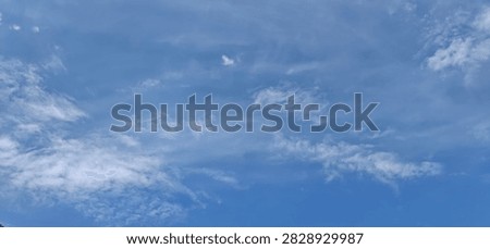 Wide angle view of bright blue sky with soft white clouds, ideal natural background texture for graphic design.