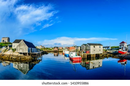 A wide angle view of a calm summer evening in the fishing village of Peggys Cove, Nova Scotia. Local buildings and boats cast mirror like reflections in the near still Atlantic Ocean. 
 - Powered by Shutterstock