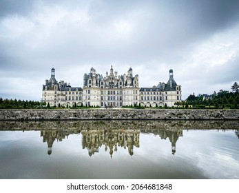 Wide Angle View Of Castle Of Chambord In Loire Valley, With Its Gardens, Cloudy Day, Water Reflection, France