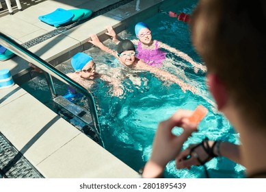 Wide angle view of children practicing swimming skills during pool lesson with instructor supervision, building water safety and confidence. Ideal for youth sports or swim school marketing