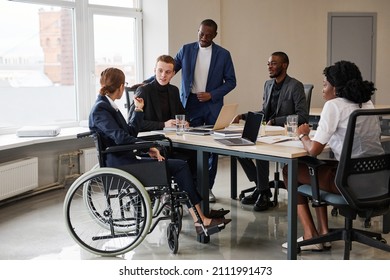 Wide Angle View At Diverse Group Of Business People At Meeting Table In Office With Woman Using Wheelchair In Foreground, Copy Space