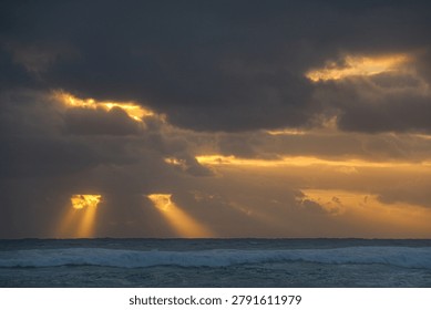 Wide angle view of a dramatic late afternoon sky over the ocean with two sunbursts and the sun shining through the clouds looking like a menacing face.