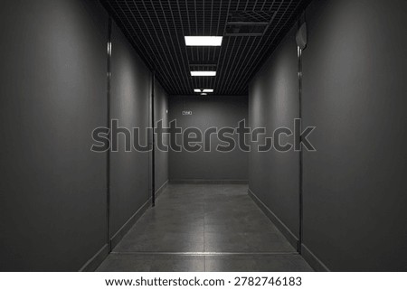 Wide angle view of empty modern corridor leading toward emergency exit sign, showing office or commercial interior circulation. Suitable for workplace safety, evacuation, access themes