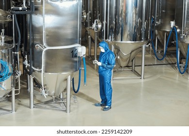 Wide angle view at factory workshop with storage tanks and worker wearing protective suit, copy space - Powered by Shutterstock