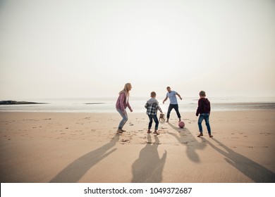 Wide Angle View Of A Family Playing Football At The Beach.