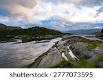 Wide angle view of a fast-flowing river through rocky terrain towards the sea with mountains in the background.