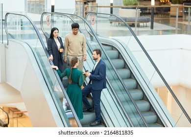 Wide angle view at group of business people standing on escalator in office building and communicating, copy space - Powered by Shutterstock