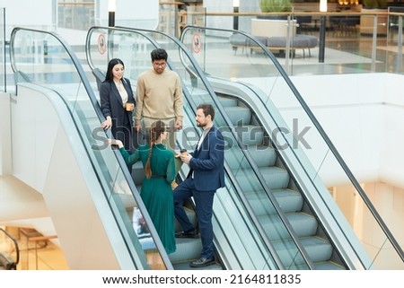 Wide angle view at group of business people standing on escalator in office building and communicating, copy space