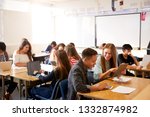 Wide Angle View Of High School Students Sitting At Desks In Classroom Using Laptops