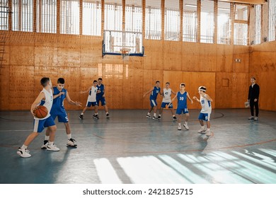 Wide angle view of junior basketball players playing and practicing basketball with their trainer at an indoor court. Basketball kids learning how to play basketball on court during their training. - Powered by Shutterstock