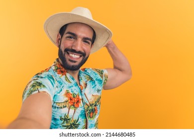 Wide Angle View Of A Latin Young Man Wearing Summer Clothes Extending His Arm And Taking A Selfie While Holding His Hat. High Quality Photo