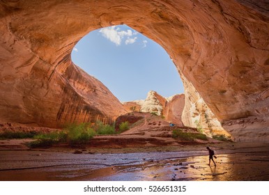 Wide Angle View Of Male Hiker Backpacking Beneath Stunning Jacob Hamblin Arch In Coyote Gulch On A Sunny Day With Blue Sky And Clouds In Summer, Grand Staircase-Escalante National Monument, Utah, USA