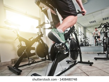 Wide Angle View Of Man In Sports Sneakers And Shorts Does Exercises On Cardio Bike At Spinning Class. Healthy Lifestyle Concept