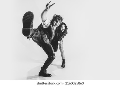 Wide angle view. Monochrome portrait of crazy musicians, young boy and girl wearing black leather outfits moving on white studio background. Concept of style, art, fashion and youth, ad