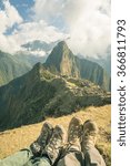 Wide angle view on Machu Picchu from the terraces above. Foots and hiking boots out of focus in the foreground. Toned image, vintage old retro filter.
