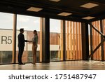 Wide angle view of real estate agent shaking hands with client while standing in empty office building interior lit by sunlight, copy space