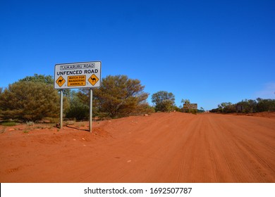 Wide Angle View Of The Red Dust Road Towards Western Australia With Road Signs Warning Of Camels Wandering Around; Northern Territory, Australia