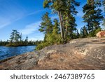 Wide angle view of a rocky shore with pines on a blue northern Minnesota lake 