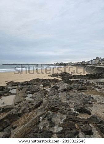Wide angle view of rugged dark coastal rocks on a sandy beach under an overcast sky in Saint-Malo, Brittany, France, for travel tourism and nature background copy space.