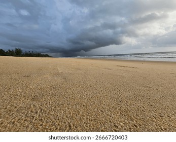 Wide angle view of a sandy beach with ocean waves and dramatic blue clouds in the sky