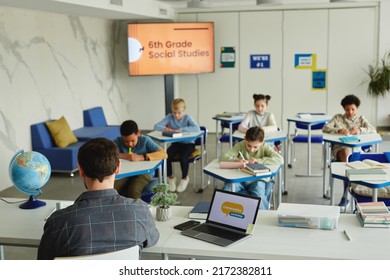 Wide Angle View At School Classroom With Diverse Group Of Children Taking Test, Male Teacher In Foreground, Copy Space