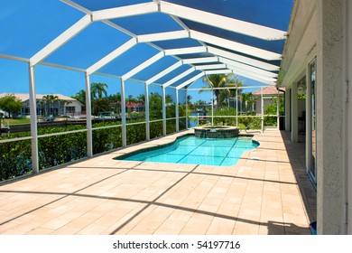 Wide Angle View Of Screened In Pool And Lanai In Florida With Blue Sky And Canal