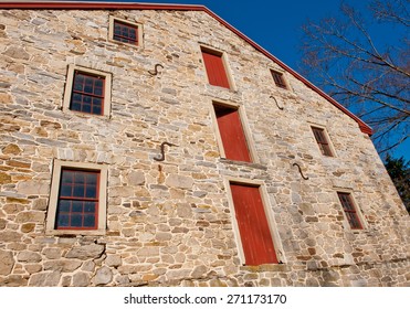 Wide angle view of side of stone barn building with red doors and windows against blue sky.