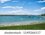 Wide angle view standing on a grassy field looking out onto the lake filled with sailboats. Sunny summer day with cloudy blue skies and lush green grass.  Taken at the Glenmore Reservoir in Calgary.