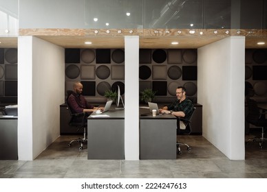 Wide angle view of two freelance business men working in cubicle styled co working office space.