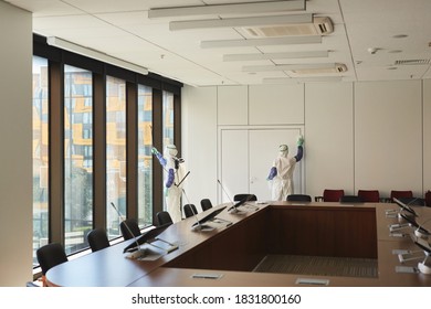 Wide angle view at two sanitation workers wearing hazmat suits disinfecting conference room in office, copy space - Powered by Shutterstock