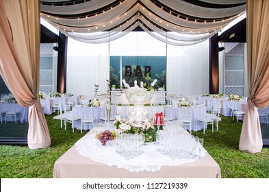 A Wide Angle View Of A Wedding Reception Venue, With Dance Floor And Surrounding Tables. A Large Chandelier In The Middle Of The Room Has Tooling Draped From It, With Mini Lights.