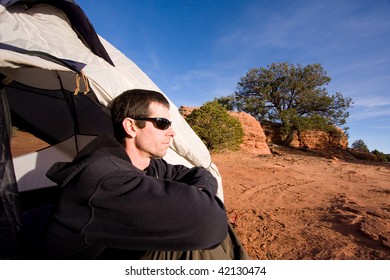 Wide angle view of young man sitting inside tent in Arizona desert. Outdoor adventure/camping concept.