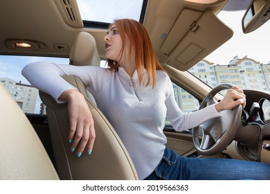 Wide Angle View Of Young Redhead Woman Driver Driving A Car Backwards Looking Behind.