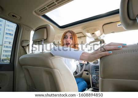Wide angle view of young redhead woman driver driving a car backwards looking behind.
