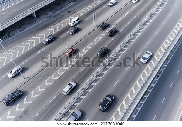 A wide asphalt road with white markings
in the center with a dense stream of cars traveling at high speed
in a big city. Aerial view taken from
drone