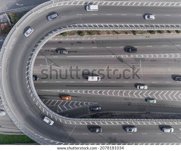 A wide asphalt road with white markings\
in the center with a dense stream of cars traveling at high speed\
in a big city. Aerial view taken from\
drone