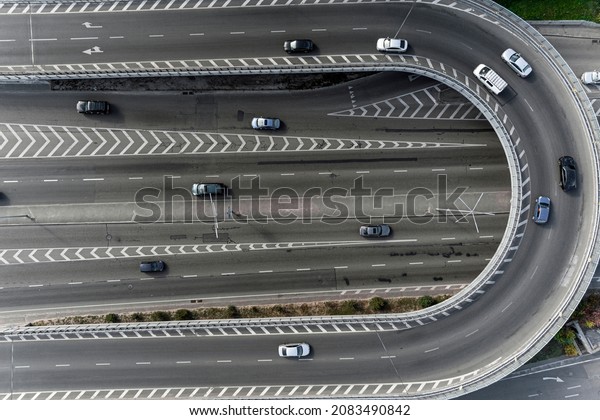 A wide asphalt road with white markings\
in the center with a dense stream of cars traveling at high speed\
in a big city. Aerial view taken from\
drone