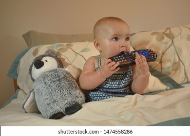 Wide Awake 7 Month Old Baby Girl Playing With Remote And Watching TV In Parent's Bed At Bedtime