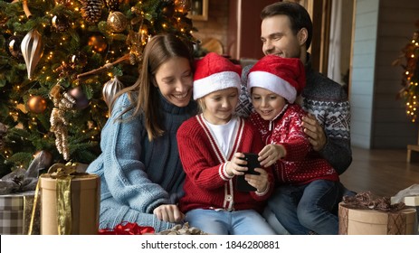 Wide Banner Header View Of Happy Young Family With Small Children Sit Near Christmas Tree Use Cellphone Together. Smiling Parents With Little Kids Enjoy Smartphone Call Greet With New Year Online.