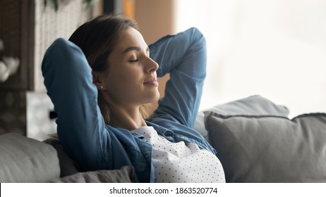 Wide banner panoramic view of happy young Caucasian woman sit rest on couch sleep or take nap. Calm millennial female relax on sofa in living room, breathe fresh air, relieve negative emotions.