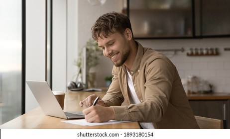 Wide banner panoramic view of smiling young Caucasian man sit at desk make notes working online on computer. Happy millennial male handwrite study distant on laptop in office. Education concept. - Powered by Shutterstock
