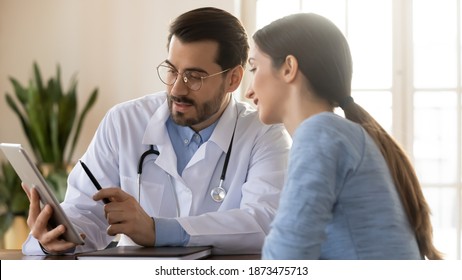 Wide banner panoramic view of young male GP use tablet discuss illness anamnesis to female patient at meeting. Man doctor and woman client look at pad screen consider test results on gadget. - Shutterstock ID 1873475713