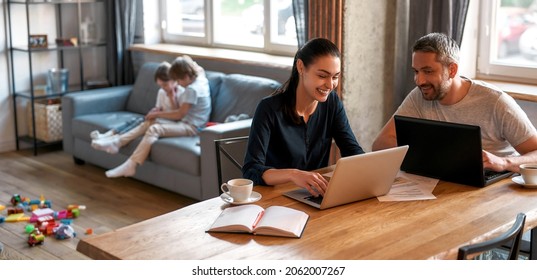 Wide banner view of happy young Caucasian parents couple sit at table at home work online on laptops. Smiling mother and father stay at home freelance on computer. Distant job, lockdown. - Powered by Shutterstock