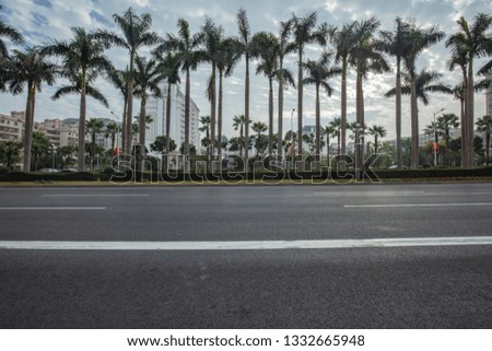 Wide black asphalt pavement in the city, tall coconut tree green belt, blue sky and white clouds background, the car flew past to form a virtual dynamic.