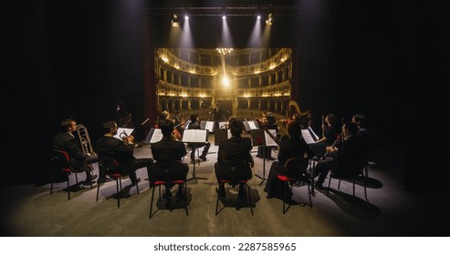 Wide Cinematic shot of Conductor Directing Symphony Orchestra with Performers Playing Violins, Cello and Trumpet on Classic Theatre with Curtain Stage During Music Concert. Back View - Shutterstock ID 2287585965