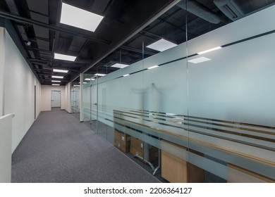 A wide corridor of a modern office with furniture behind glass partitions.