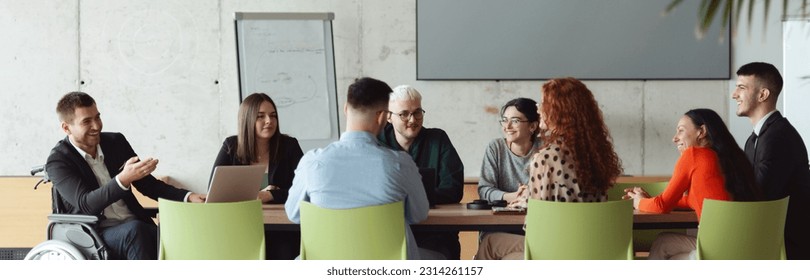 Wide crop photo of a diverse group of business professionals, including an person with a disability, gathered at a modern office for a productive and inclusive meeting. - Powered by Shutterstock