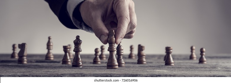 Wide cropped image of a human hand wearing business suit moving dark King chess piece at table, toned retro effect.